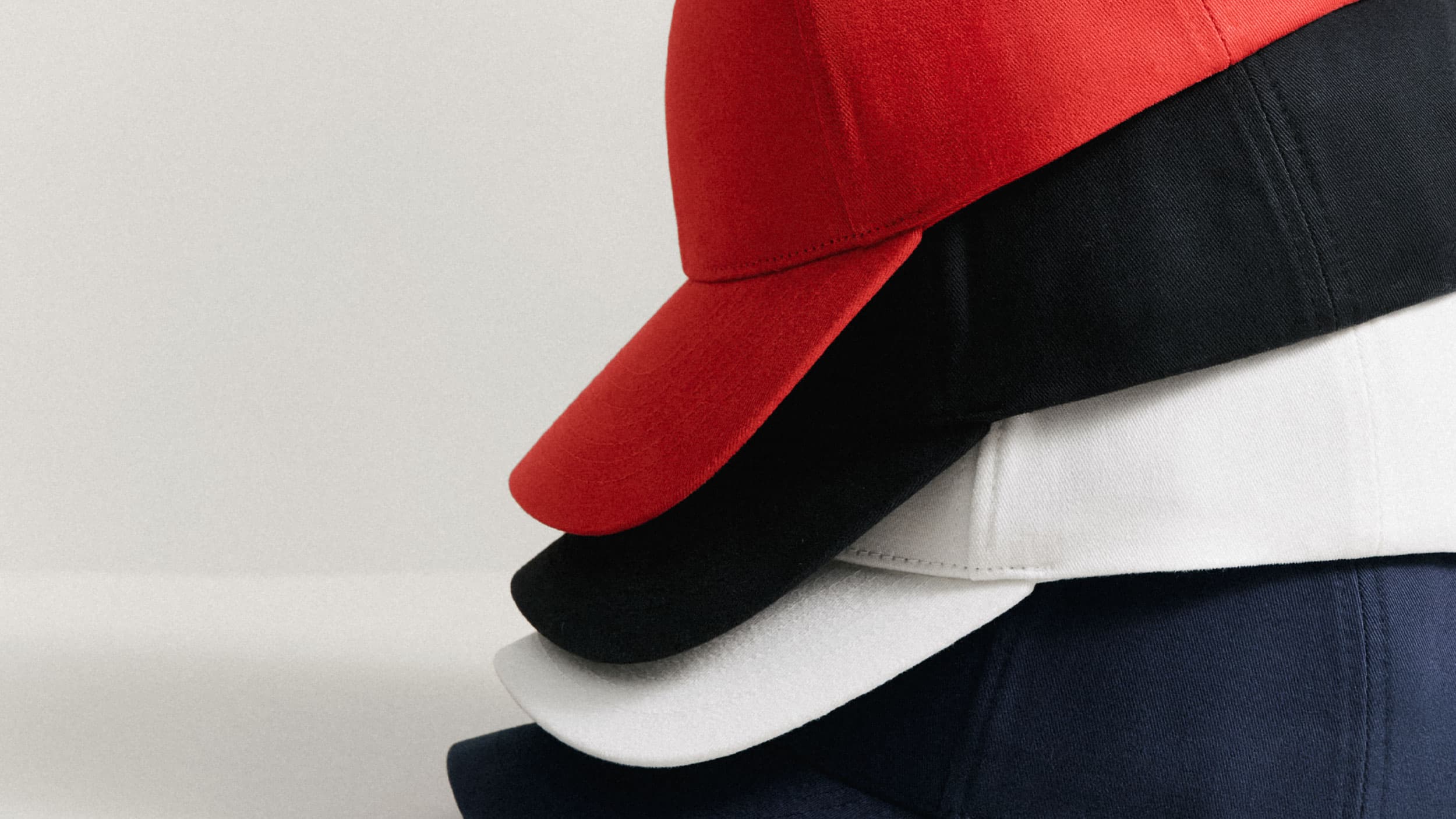 A stack of four caps in red, black, white, and navy blue, layered neatly against a plain background.