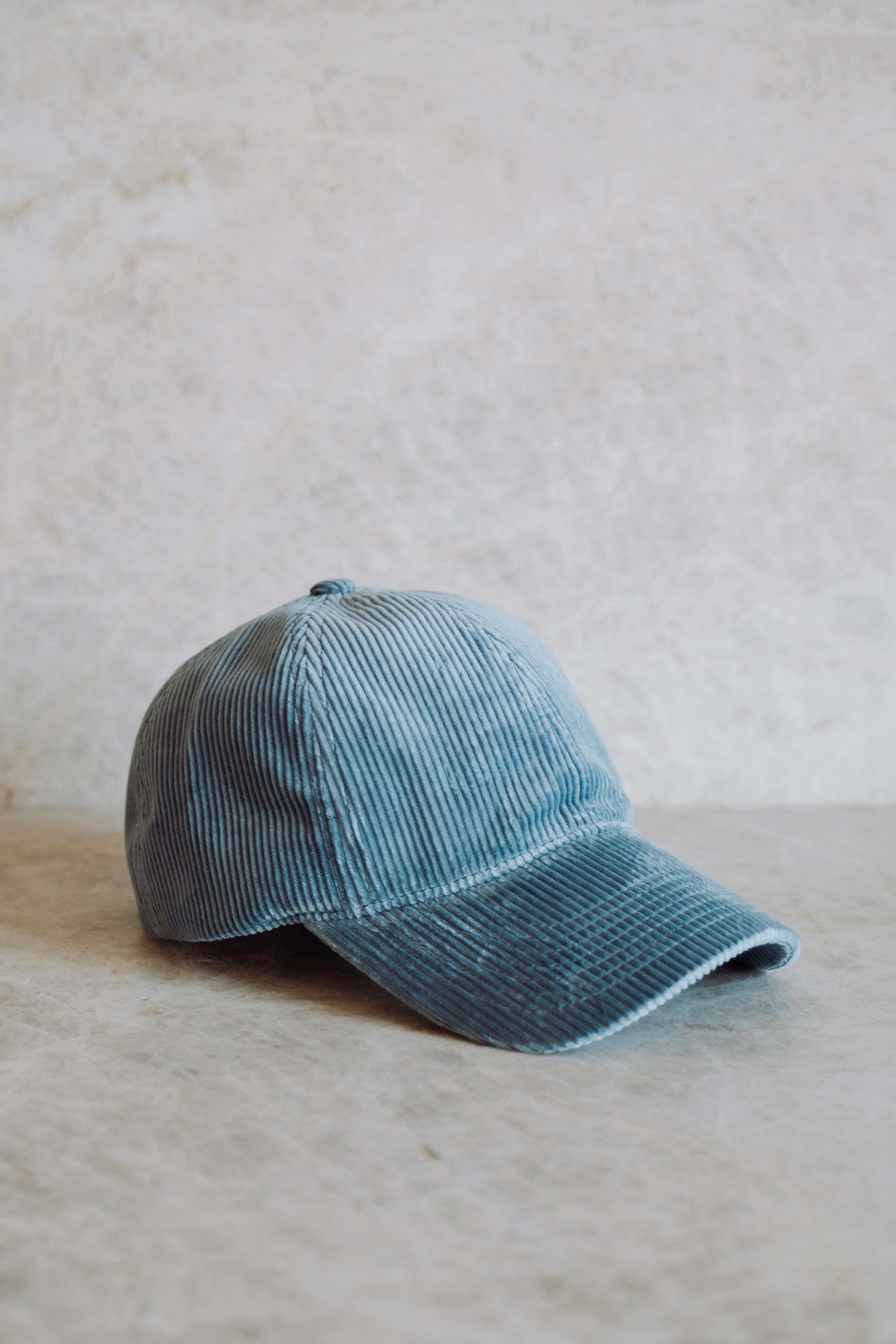 Light blue corduroy baseball cap on a textured gray surface, viewed from the side.