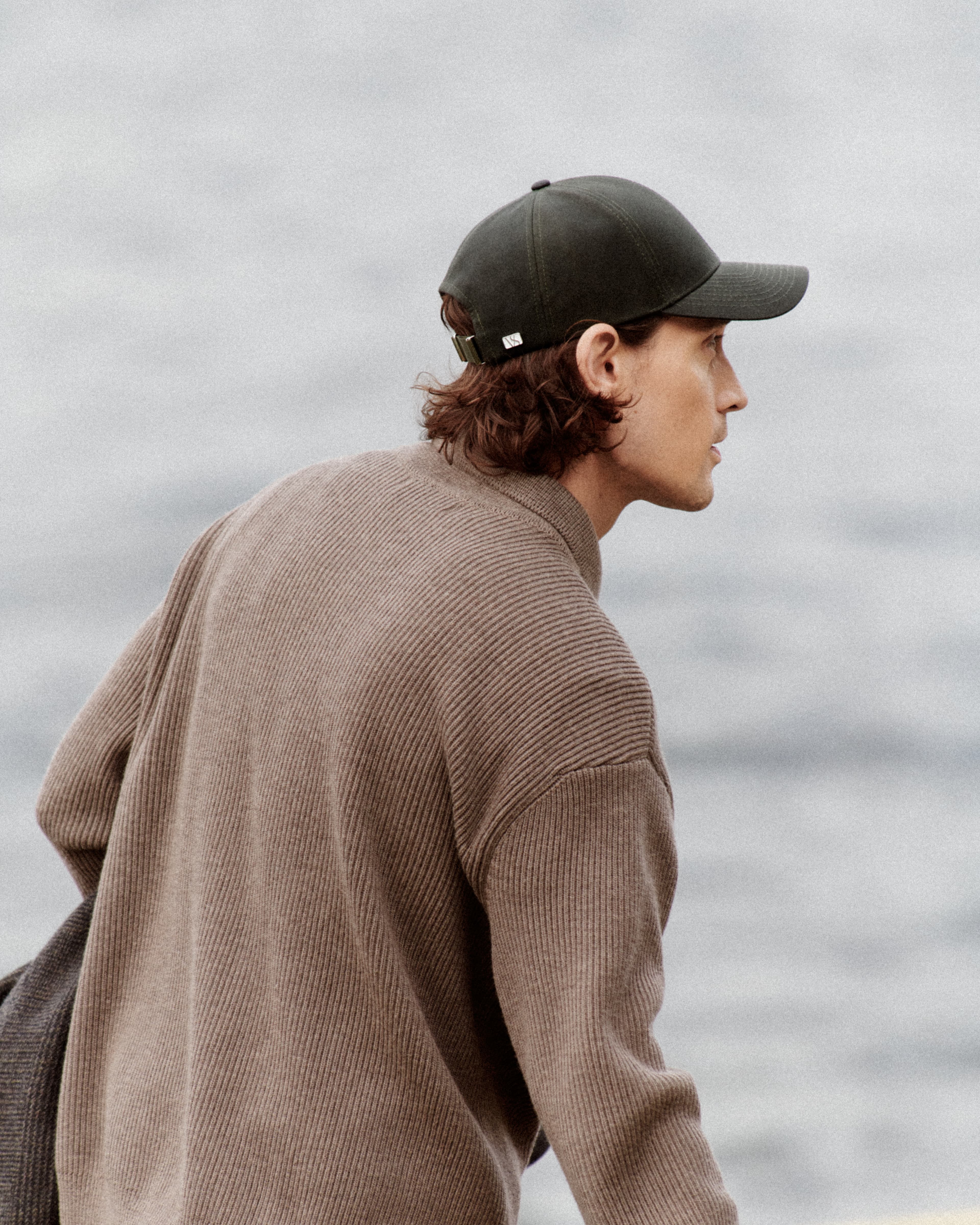 Side view of a male model wearing a green oilskin cap from varsity headwear