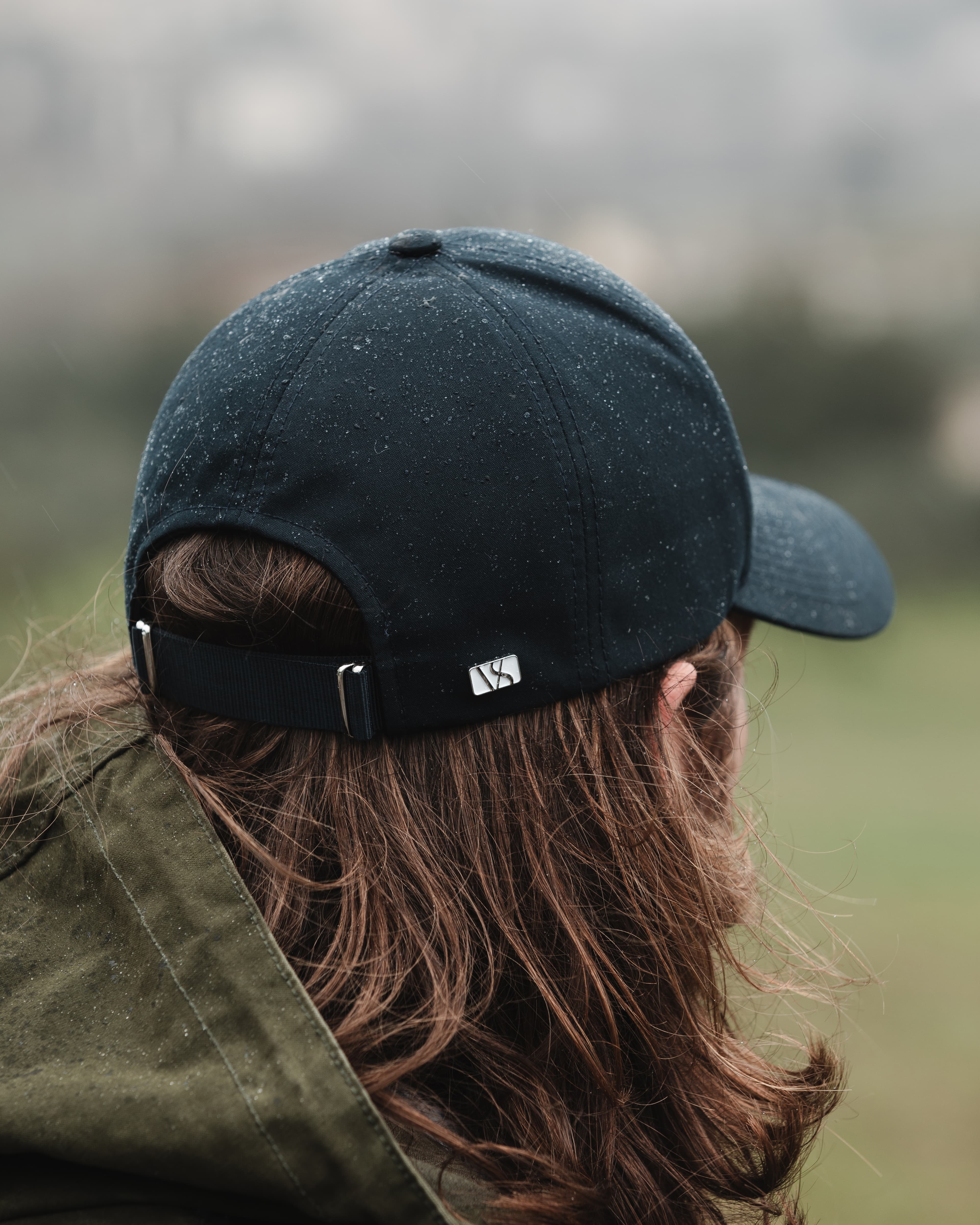 Back view of a black varsity headwear cap on male model in outdoor rainy environment